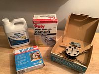 Various handyman and house repair items including rust remover, concrete patch, caulking cord, and a power stripper tool in its box on a wooden surface.