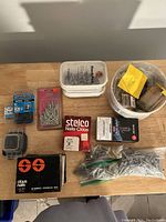 Photo showing multiple packages and containers of nails and screws on wooden surface.