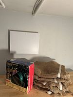 Photo showing stacked burlap wraps next to the boxed clothesline kit with visible label