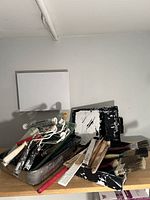 A general view showing five paint trays and multiple paint brushes in various sizes and styles with paint residue, placed on a wooden surface against a wall.