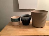 Front view of three pots: medium ceramic blue/white, small ceramic teal/beige, large beige plastic ribbed pot