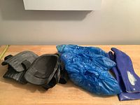 Grey knee pads, blue disposable booties, and purple rubber gloves laid out on a flat surface.