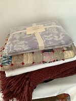 Stacked assorted throws including a packaged woven damask throw.