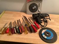 Electric drill lying next to multiple screwdrivers with red, yellow, black, and wooden handles.