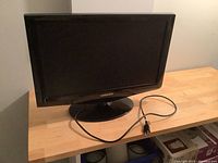 Front view of the Samsung 22-inch TV showing screen, bezel, branded logo, and attached power cord on wooden table.