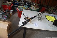 Two fishing rods laid horizontally on a white table alongside other items in garage setting