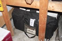 Black Colorado 800DLX tent carrying bag under wooden stairs on concrete floor