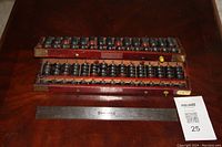 Pair of large and smaller wooden Chinese abacuses placed on a wooden surface with a ruler for scale, tags visible indicating lot number