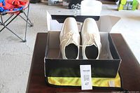 Top-down view of pair of white men's dress shoes in original box on table in garage setting.