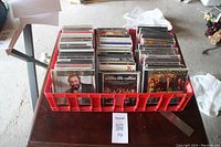 Red plastic crate filled with multiple rows of CDs, front view shows album covers of José Carreras and Shenandoah among others.