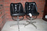 Pair of two black leather office chairs with padded seats and backs, tufted button detailing, and chrome swivel bases ending with casters.
