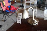 Metal desk lamp on a table with a curved neck and dome-shaped shade with brushed metal finish