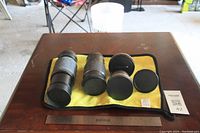 Five camera lenses arranged on a yellow cloth showing the lenses from the front with caps on.