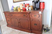 Full front view of the solid hardwood cupboard with varied drawers and cabinet doors. Top surface has several household items placed.