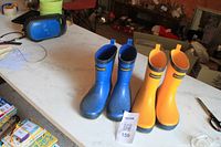 Two pairs of kids' rain boots, one blue and one yellow, displayed side by side on a table with a tag showing number 159.