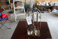 Five stainless steel kitchen utensils hanging on a metal stand, placed on a dark wood table in a warehouse setting.