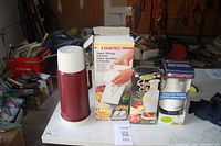 Red thermos and three boxed Starfrit kitchen tools arranged on a white surface in a garage setting.