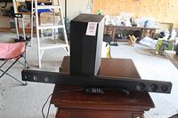 Wide shot of LG sound bar, wireless subwoofer, and remote on wooden table in large room