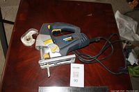 Front angle shot of the electric jigsaw on wooden surface showing power cord and blade.