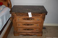 Front view of one wooden night stand showing intricate carved details and marble top.