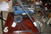 Side view of the blue Simoniz 1600 PSI electric pressure washer, showing the spray wand and power cord coiled around the unit on a wooden surface.