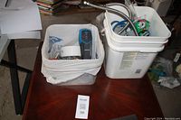 Photo of two white plastic buckets on wood table containing assorted hardware, stud finder visible.