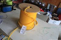 Large wooden spool of bright yellow twisted polypropylene rope on a table in a workshop or storage area.