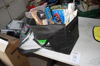 Photo of black fabric carry bag filled with various tools and hardware items on a white table