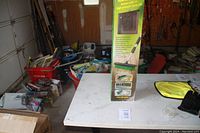 Photo showing the front view of the Ultimate Water Broom 2 in 1 box standing on a white table in a garage-like setting with various items around.