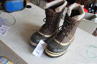 Front and side view of brown winter boots on table showing lace-up design and shearling lining.