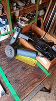 Mastercraft angle grinder and Black & Decker drill on a wooden workbench with tools and shelves in background.