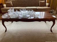 Full view of the wood coffee table showing queen anne legs and scalloped edges with cut glassware on top.