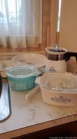 Photo showing entire set of Corning Blue Cornflower coffee pot, casserole, pie plates, baking dish, and Pyrex Butterprint turquoise dish.