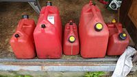 Five red plastic gas cans in a row of varying sizes with black and yellow caps.