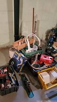 Wide shot showing various tools, wire coil, basket with tiles, and other supplies on basement floor.