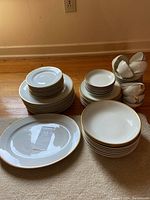 Full view of entire Limoges china partial set arranged on the floor showing stacked plates, bowls, cups and saucers, and two large serving platters.