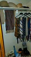 Men's ties hanging on a rod in assorted patterns and colors including floral and stripes, with a scarf hanging on the left side.