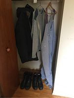Coat, gray jacket, and striped bib overalls hanging on hooks with two pairs of black boots on floor