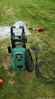Full front view of green and black Certified pressure washer unit with hose and spray gun placed on grass.