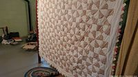Full view of handmade quilt hanging showing repeating pinwheel blocks, floral and white fabric, and triangle trim on edge.