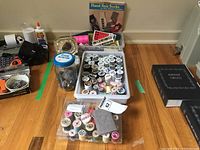 Wide view of assorted sewing supplies including various spools of thread in plastic containers, jars of buttons or pins, and a book on hand knit socks.