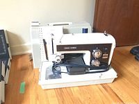 Full view of Sears Kenmore sewing machine with carry case and power cord laid on wooden floor.