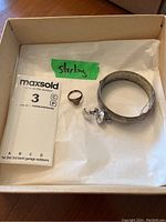 Box containing the sterling silver bangle bracelet, signet ring, and screw-back earrings labeled with green tape 'sterling'.