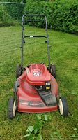 Front and top view of Toro lawn mower with red body, black handle, and four wheels on grass.