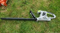 Side view of Earth Wise electric hedge trimmer lying on grass showing the full length and blade guard.