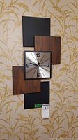 Front view of 70s style wall clock with wood grain and black panel backing on patterned wallpaper.