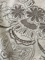Close-up of tablecloth embroidery showing cutwork and satin stitch details in floral and butterfly patterns on ecru fabric