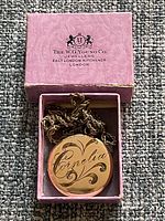 Antique gold-tone round locket necklace in a pink box from W.G. Young Co., engraved with 'Cornelia'.