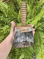 Front view showing overall shape, wooden beehive handle and metal scoop of the antique seed shuttle held in hand.