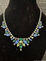 Front view of vintage lavaliere necklace displayed on black velvet bust showing the hand set coloured stones in blue, green and light green with silver-tone setting.